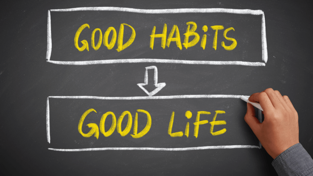 Ręka pisząca na tablicy kredowej hasło „Good Habits → Good Life” żółtą kredą