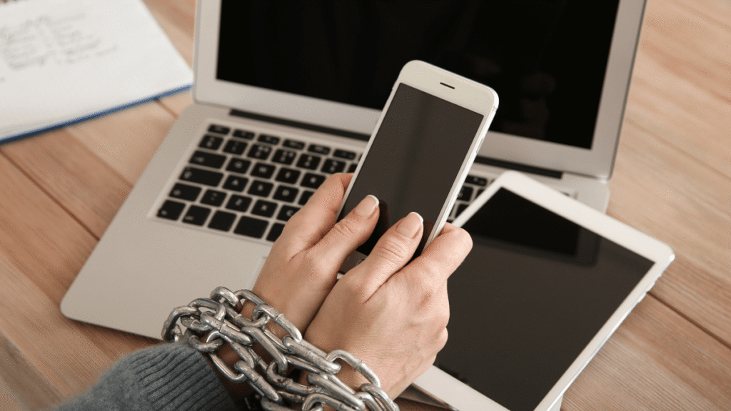 Ręce w łańcuchach trzymające smartfona, symboliczne przedstawienie uzależnienia od urządzeń cyfrowych